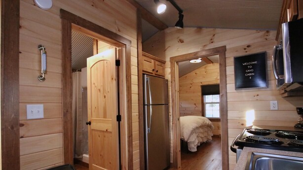 A cabin interior with a wooden interior, a refrigerator, a stove, and a bed.