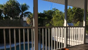 A wooden deck with a view of a swimming pool and palm trees. - Secluded and Private House with Pool, Near Beach.  11 blocks from Village. (Boca Grande)
