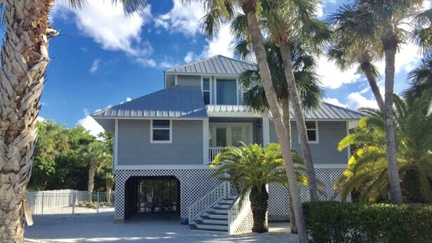 A two-story house with a covered porch, a small staircase, and a gravel driveway. - Secluded and Private House with Pool, Near Beach.  11 blocks from Village. (Boca Grande)