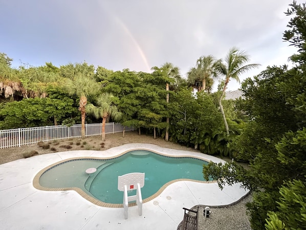 Una piscina con una silla blanca, rodeada de abundante follaje y una valla blanca.