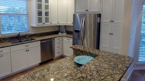A kitchen with white cabinets, a stainless steel refrigerator, granite countertops, and a built-in dishwasher. - Secluded and Private House with Pool, Near Beach.  11 blocks from Village. (Boca Grande)