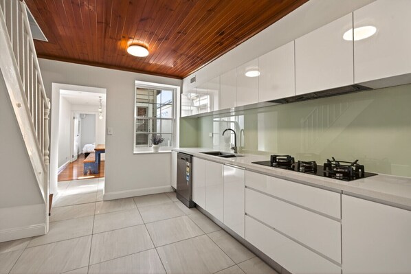 A modern kitchen with white cabinetry, a wooden ceiling, and a view into the adjacent bedroom.