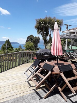 Een houten terras met lounge fauteuils en een overdekte tafel, met uitzicht op een waterpartij en heuvels.