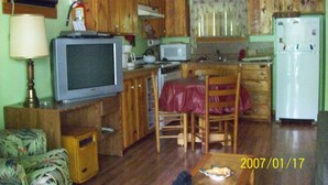 A compact kitchen with wooden cabinets, a microwave, a refrigerator, and a dining area with a table and chairs. - Sanitized! Creekside Cottage sits over Creek  Woods, Looking into Park!  Pets OK (Cosby)