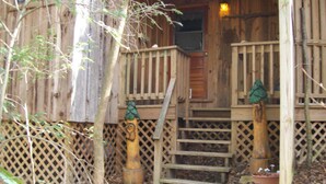 A wooden cabin with a wooden porch, a wooden staircase, and a small garden area with a potted plant. - Sanitized! Creekside Cottage sits over Creek  Woods, Looking into Park!  Pets OK (Cosby)