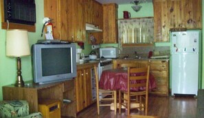 Een compacte keuken met houten kastjes, een magnetron, een koelkast, en een eethoek met een tafel en stoelen.