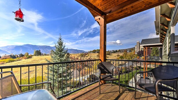 Eine Holzterrasse mit Gartenmöbeln, einem Vogelhaus und Blick auf Berge und ein Wiesenfeld.