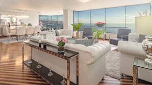 Una sala de estar moderna con un gran ventanal que ofrece vistas a la ciudad, un comedor con candelabro y un rincón de descanso acogedor.