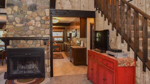 A stone fireplace, a wooden staircase, and a kitchen area with cabinets and a television. - GORGEOUS Home with Mtn Views/Perfect For Families & Groups/Wrap Porch/ATV Pking (Red River)
