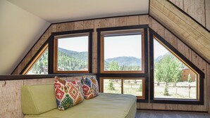 A room with a sloped ceiling and large windows offering a view of a forested area and mountains. - GORGEOUS Home with Mtn Views/Perfect For Families & Groups/Wrap Porch/ATV Pking (Red River)