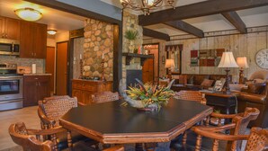 A dining area with a large table, wooden chairs, and a chandelier. There is a stone wall and wooden beams in the background. - GORGEOUS Home with Mtn Views/Perfect For Families & Groups/Wrap Porch/ATV Pking (Red River)