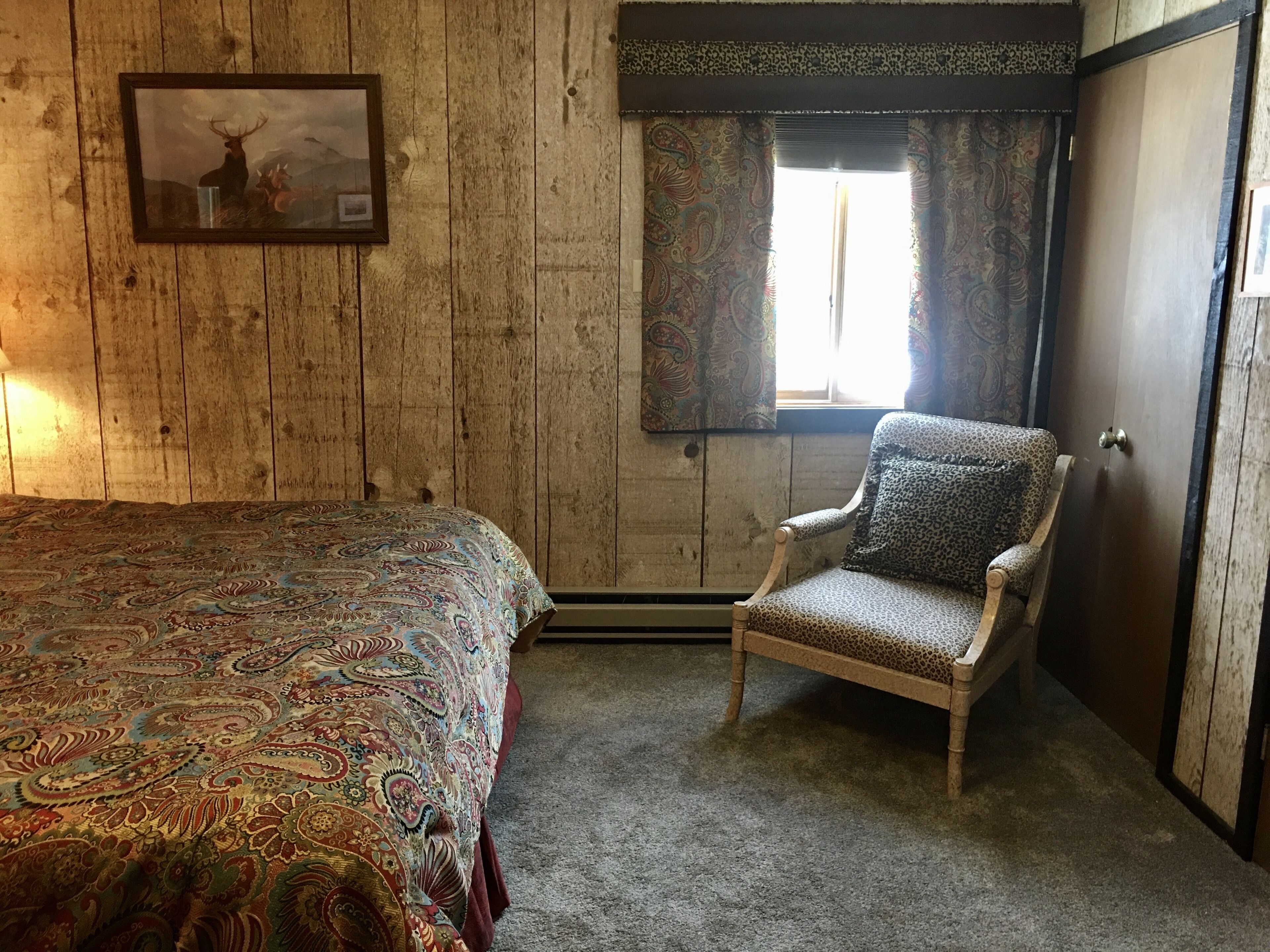 A bedroom with a bed, a chair, a window with curtains, and a door.