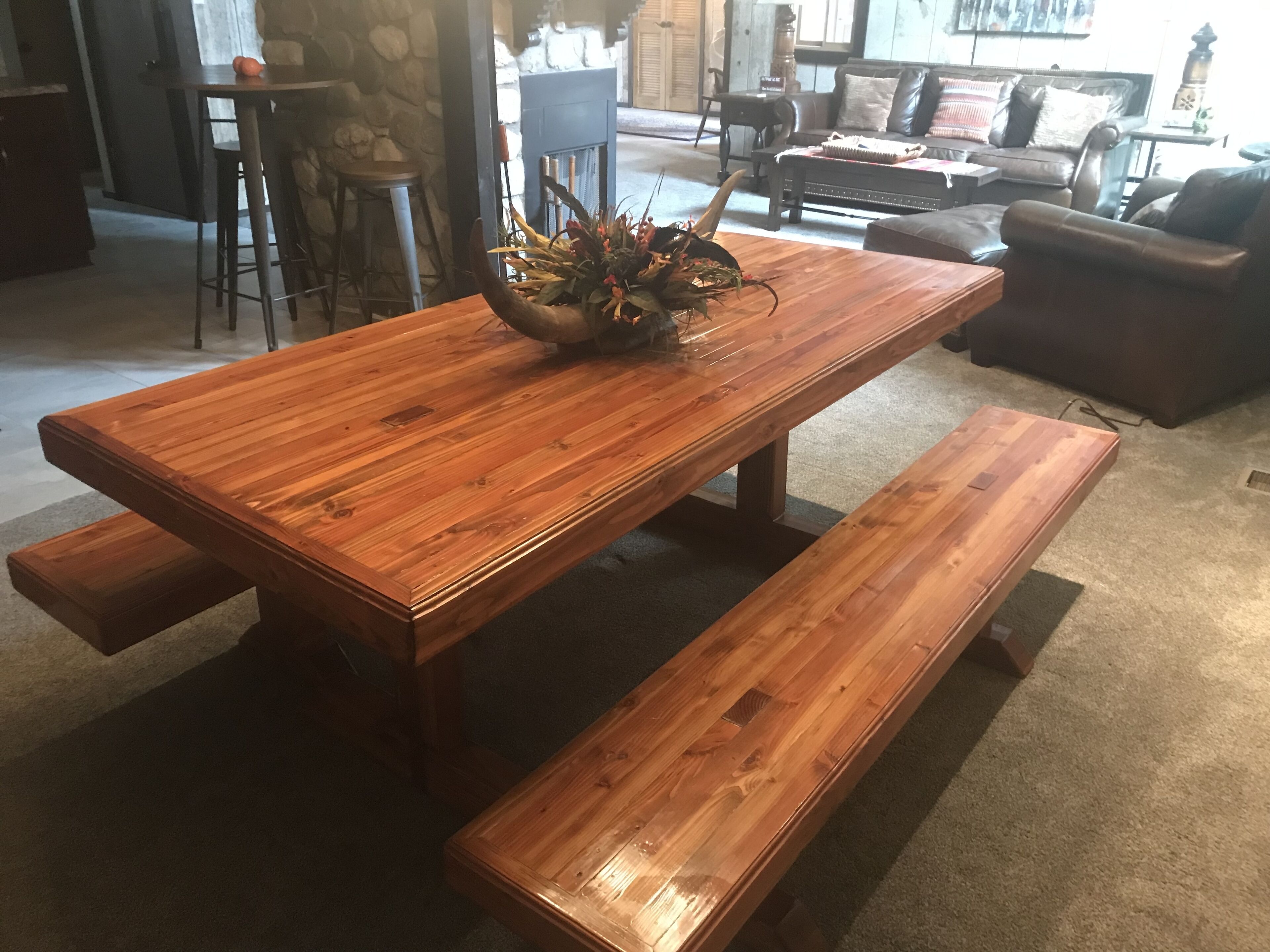 A wooden dining table with benches, a stone wall, and a sofa in the background.