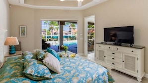 Een slaapkamer met een bed, een televisie, een dressoir en uitzicht op een zwembad.