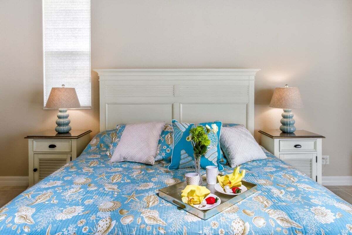 Ein Bett mit blauer Blumenbettwäsche, zwei Nachttische mit Lampen und ein Tablett mit Blumen und einer Vase auf dem Bett.