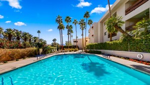 Une piscine à l’eau d’un bleu cristallin, entourée de palmiers et bordée d’un bâtiment doté de balcons.