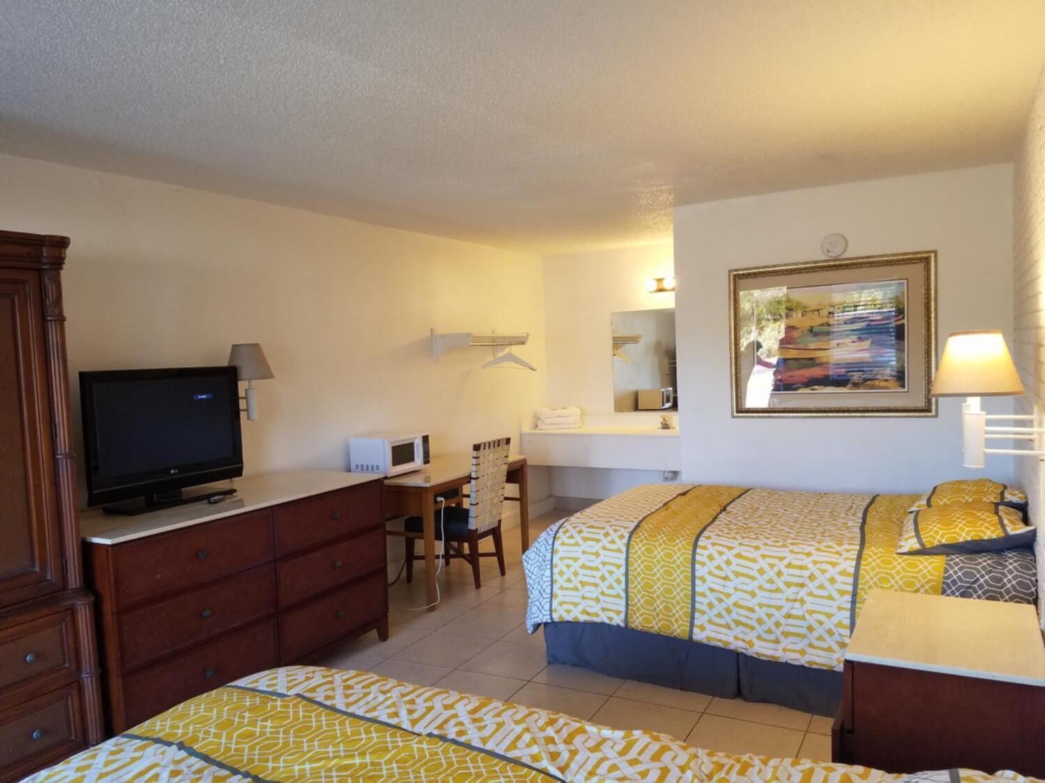 Habitación de hotel con dos camas, un televisor, un escritorio con computadora, una silla, un aparador y un baño con espejo y lavamanos.