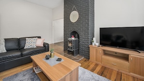 A modern living room with a black brick fireplace, a leather sofa, a wooden coffee table, and a flat-screen TV on a wooden stand.