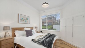 A bedroom with a bed, bedside tables, a lamp, a window with blinds, and a wardrobe.