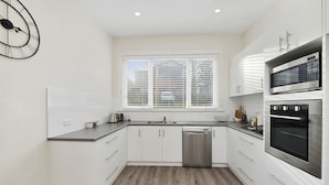 A modern kitchen with white cabinets, a stainless steel dishwasher, and a built-in oven.