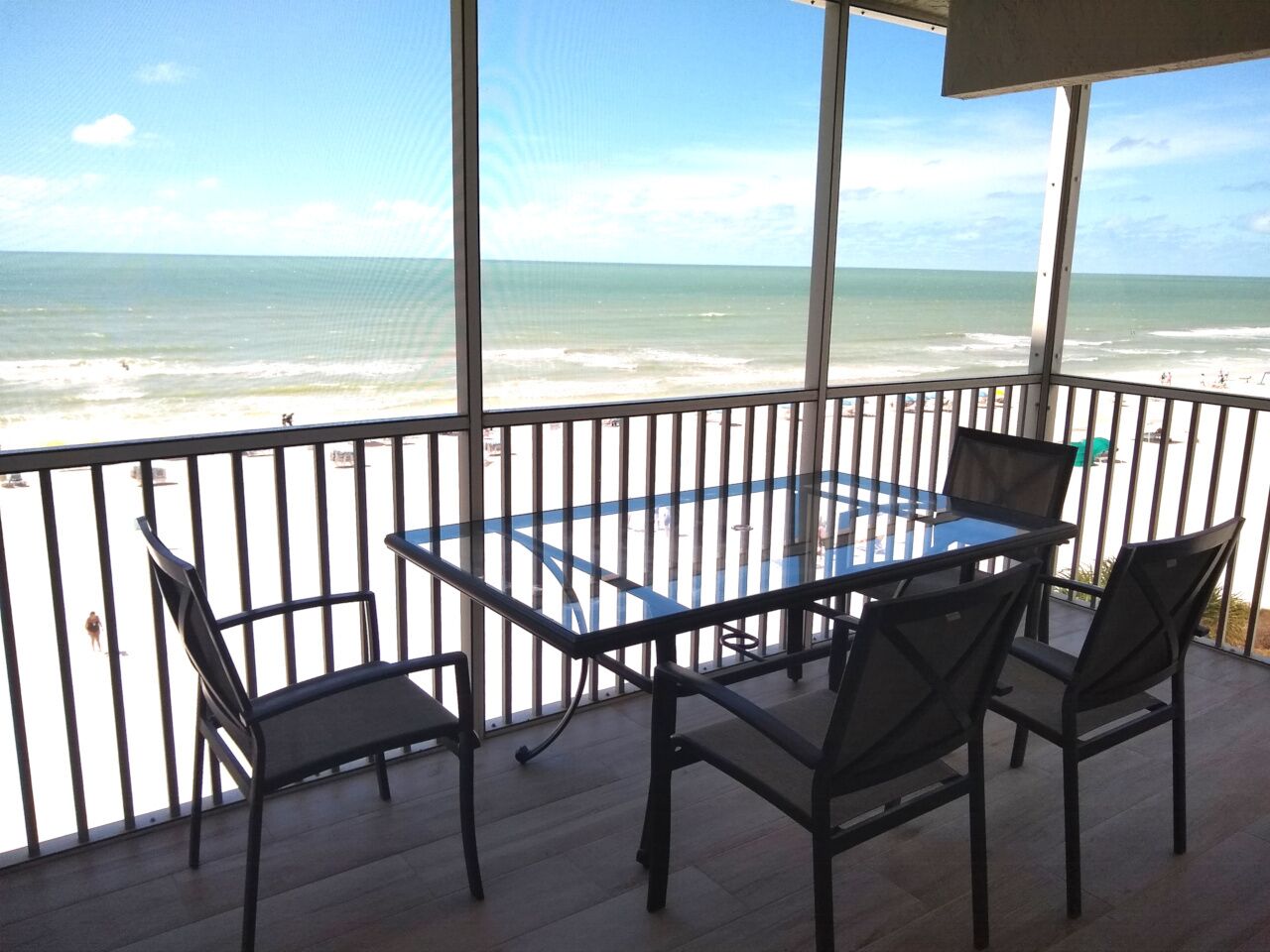 Een balkon met een glazen tafel en stoelen, met uitzicht op een strand.