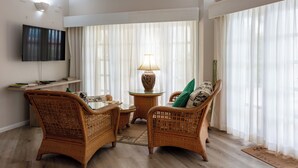 A living room with wicker furniture, a glass coffee table, a lamp, and a flat-screen TV mounted on the wall.