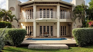 A two-story building with a pool in the front, surrounded by well-maintained hedges and a lawn.