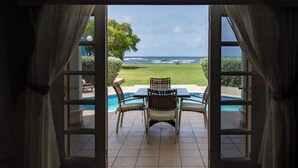 An open door leading to a patio with a table and chairs, a pool, and a view of the ocean.