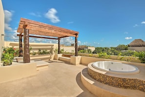 A rooftop patio with a wooden pergola, a hot tub, and a view of the surrounding landscape.