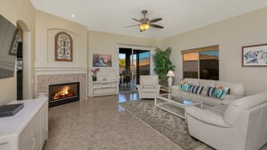 A living room with a fireplace, a ceiling fan, a sofa, and a dining area visible through a glass door.