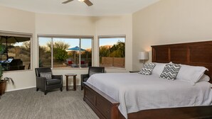 A bedroom with a large bed, two chairs, a small table, and a ceiling fan.