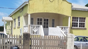 A yellow building with a white picket fence, a signboard, and a parked car. - AFFORDABLE ACCOMMODATION . VACATION SHORT OR LONG-TERM RENTALS . WELCOME TO ALL  (St. Michael)