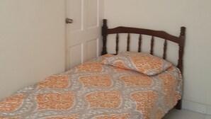 A small, single-bed room with a wooden headboard, a patterned bedspread, and a closed door. - AFFORDABLE ACCOMMODATION . VACATION SHORT OR LONG-TERM RENTALS . WELCOME TO ALL  (St. Michael)