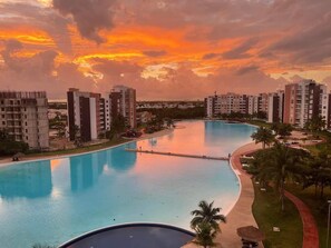 A large swimming pool with a curved design, surrounded by palm trees and a walking path.