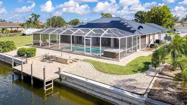 Ein Haus mit überdachter Terrasse, einem Schwimmbad und einem Steg, der ins Wasser führt.