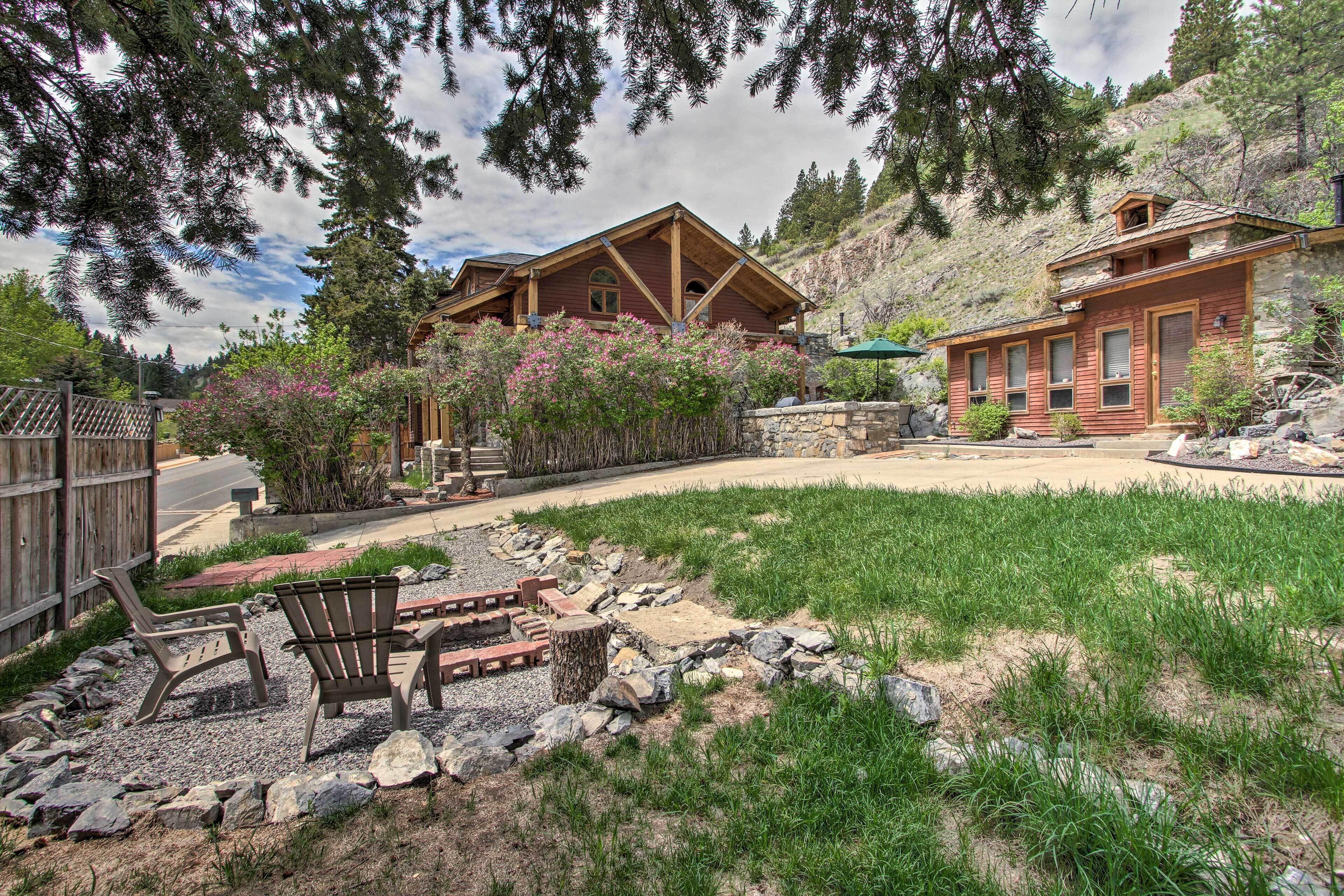 A two-story wooden cabin with a stone foundation, surrounded by a well-maintained garden and a gravel path leading to the entrance.