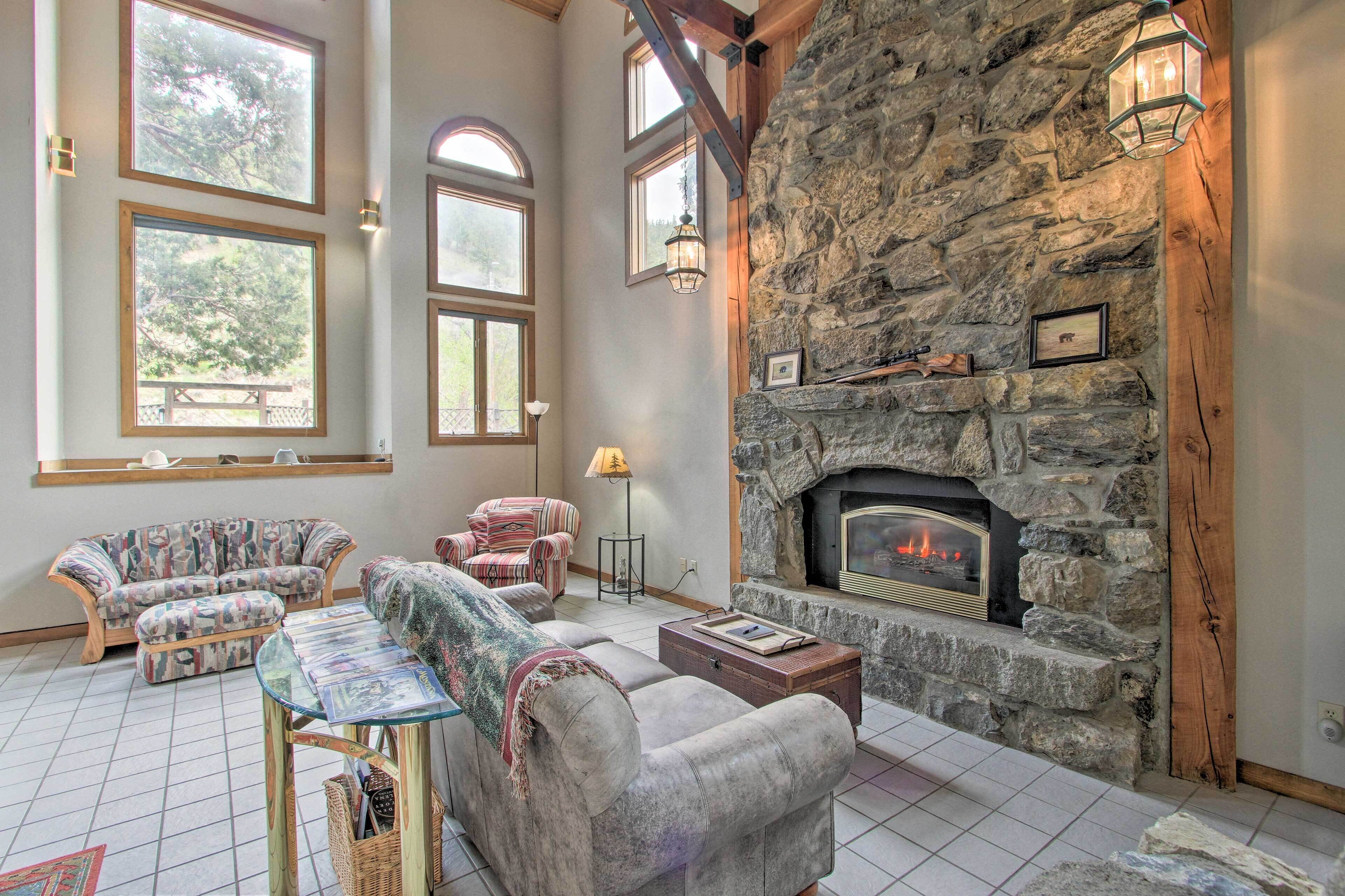 A cozy living room with a stone fireplace, large windows, and comfortable seating.