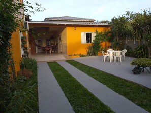 A yellow building with a covered patio, a hammock, and a table with chairs.