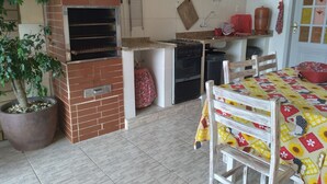 A kitchen with a brick oven, a sink, and a table with a floral tablecloth. - Complete house in Praia do Rosa (Ibiraquera)