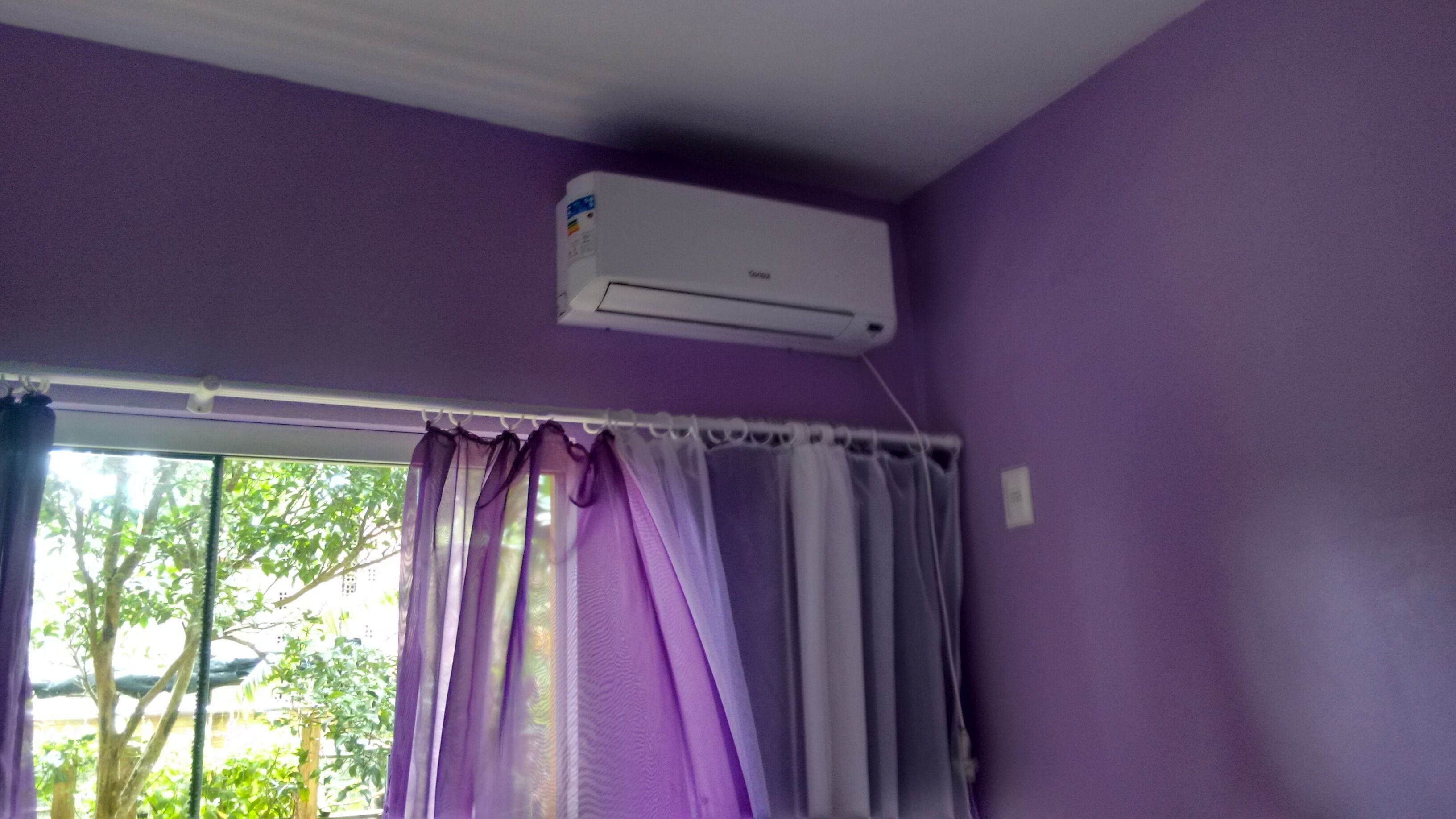 A room with purple walls, a window with purple curtains, and an air conditioning unit mounted on the wall.