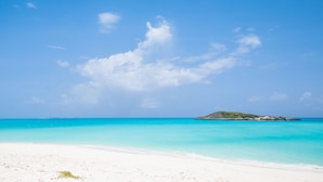 Una playa con aguas turquesas cristalinas y una pequeña isla a lo lejos.