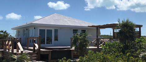 Ein Strandhaus mit Holzterrasse, überdachter Außenbereich und sandigem Weg zum Eingang.