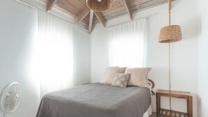 Un dormitorio con cama, mesita de noche, ventilador e lámpara colgante.