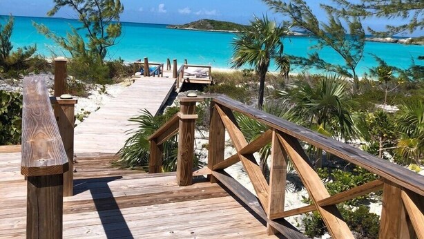 Un muelle de madera que conduce a una playa con aguas turquesas y palmeras.