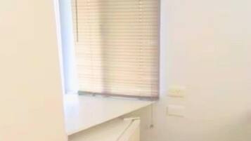 Una habitación pequeña con una ventana, un reloj en la pared y un electrodoméstico blanco.