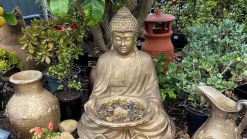 A garden statue of a seated figure with a bowl in front, surrounded by potted plants and rocks.