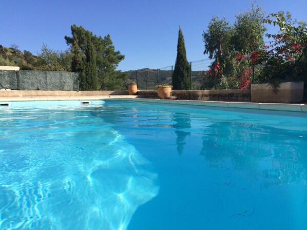 A swimming pool with clear blue water, surrounded by a stone wall and potted plants.