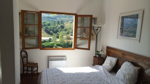 Ein Schlafzimmer mit einem Bett, einem Sessel, einem Nachttisch, einer Heizung und einem Fenster mit Blick ins Grüne.