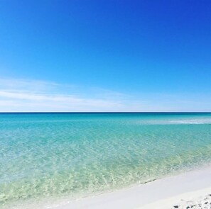 Una platja amb aigua turquesa cristal·lina i una riba de sorra blanca sota un cel blau i serè.