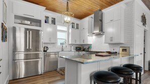 A modern kitchen with white cabinetry, stainless steel appliances, a wooden ceiling, and a central island with bar stools. - Pool | Quiet Street | Steps to Beach | Chef's Kitchen | Large Yard (Destin)
